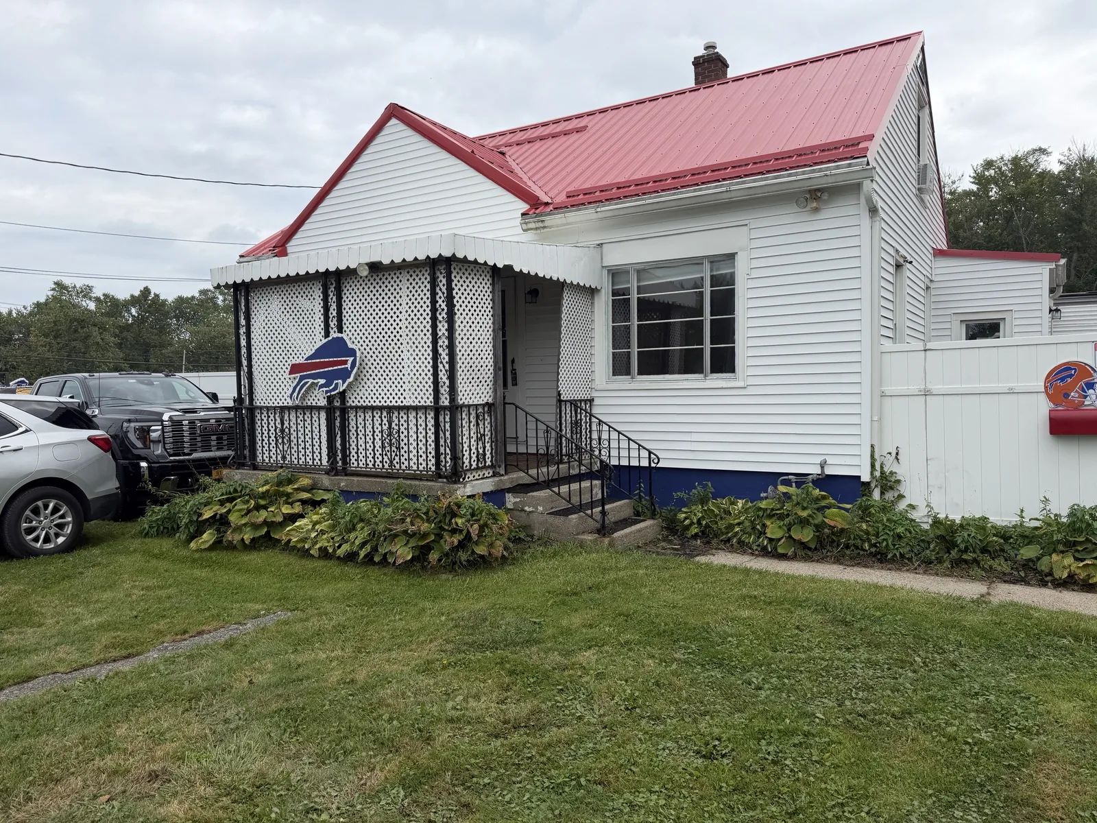 The front of the house: red metal roof, white siding, blue foundation skirt, lattice porch.
